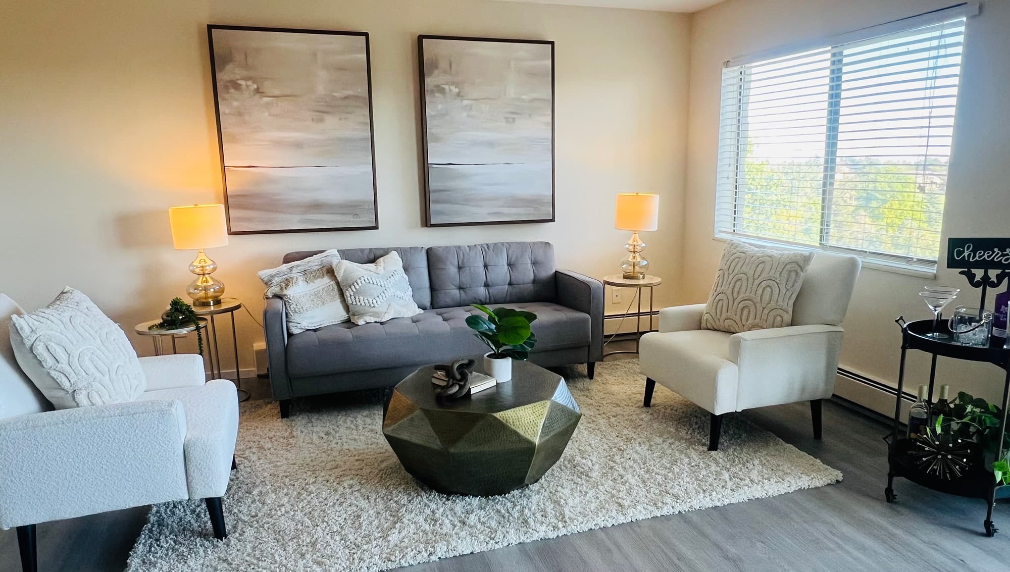 Staged apartment living room with a grey sofa, two paintings and a brass coffee table