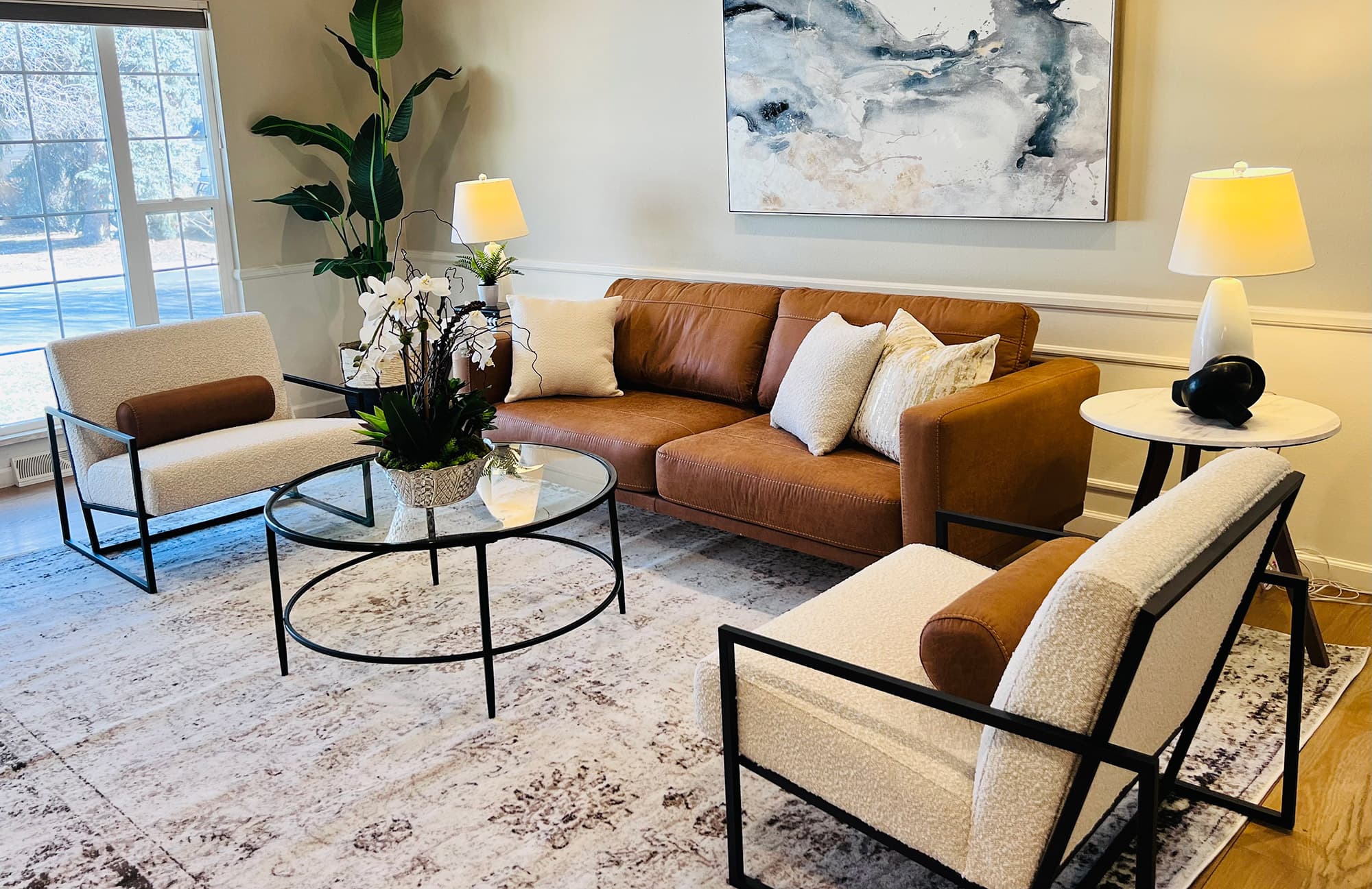 Living room staged with a cognac leather sofa, two boucle chairs, a glass coffee table and lit lamps
