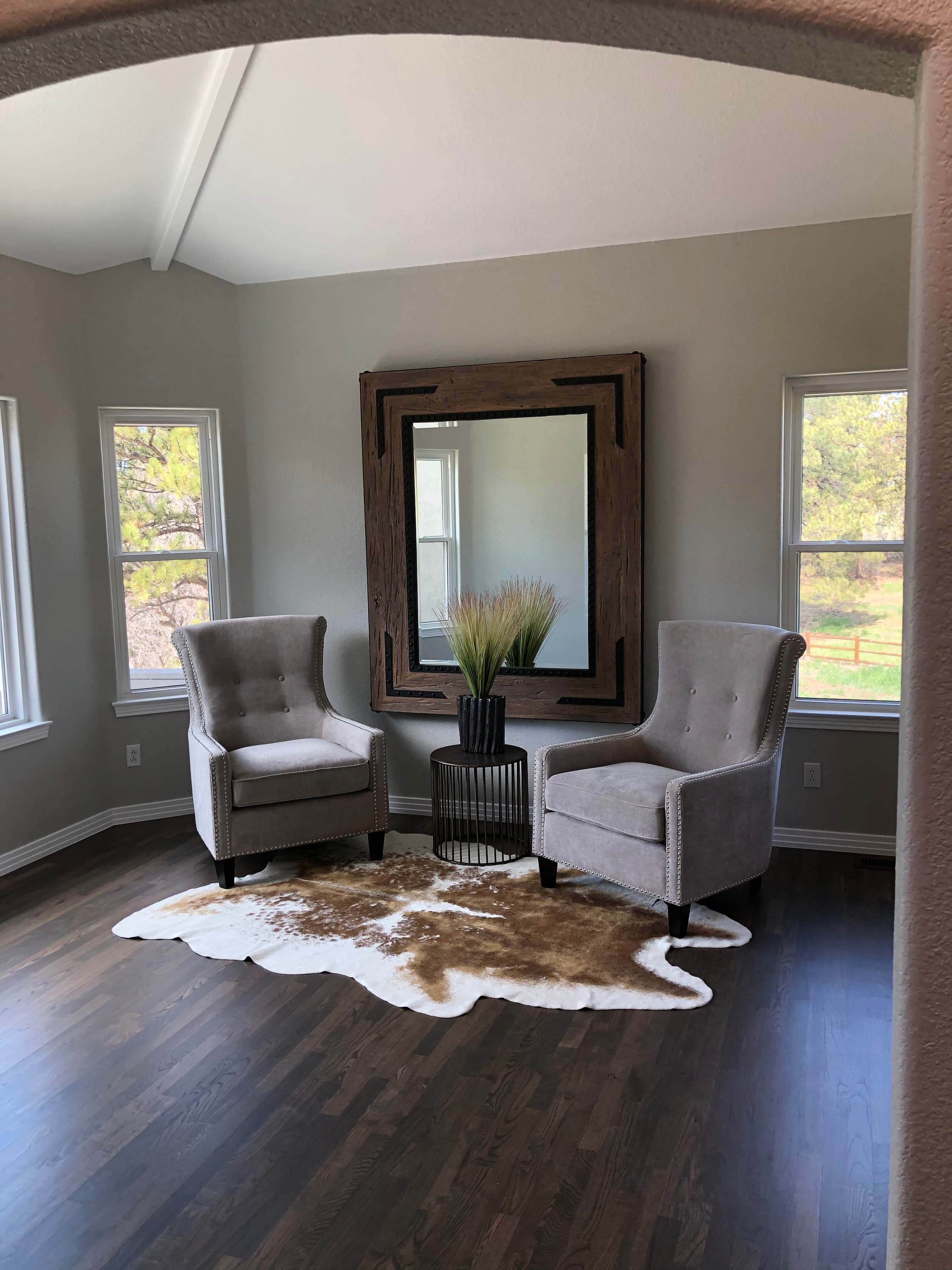 Sitting area with two grey wingback chairs, a large wood-framed mirror and a cowhide rug