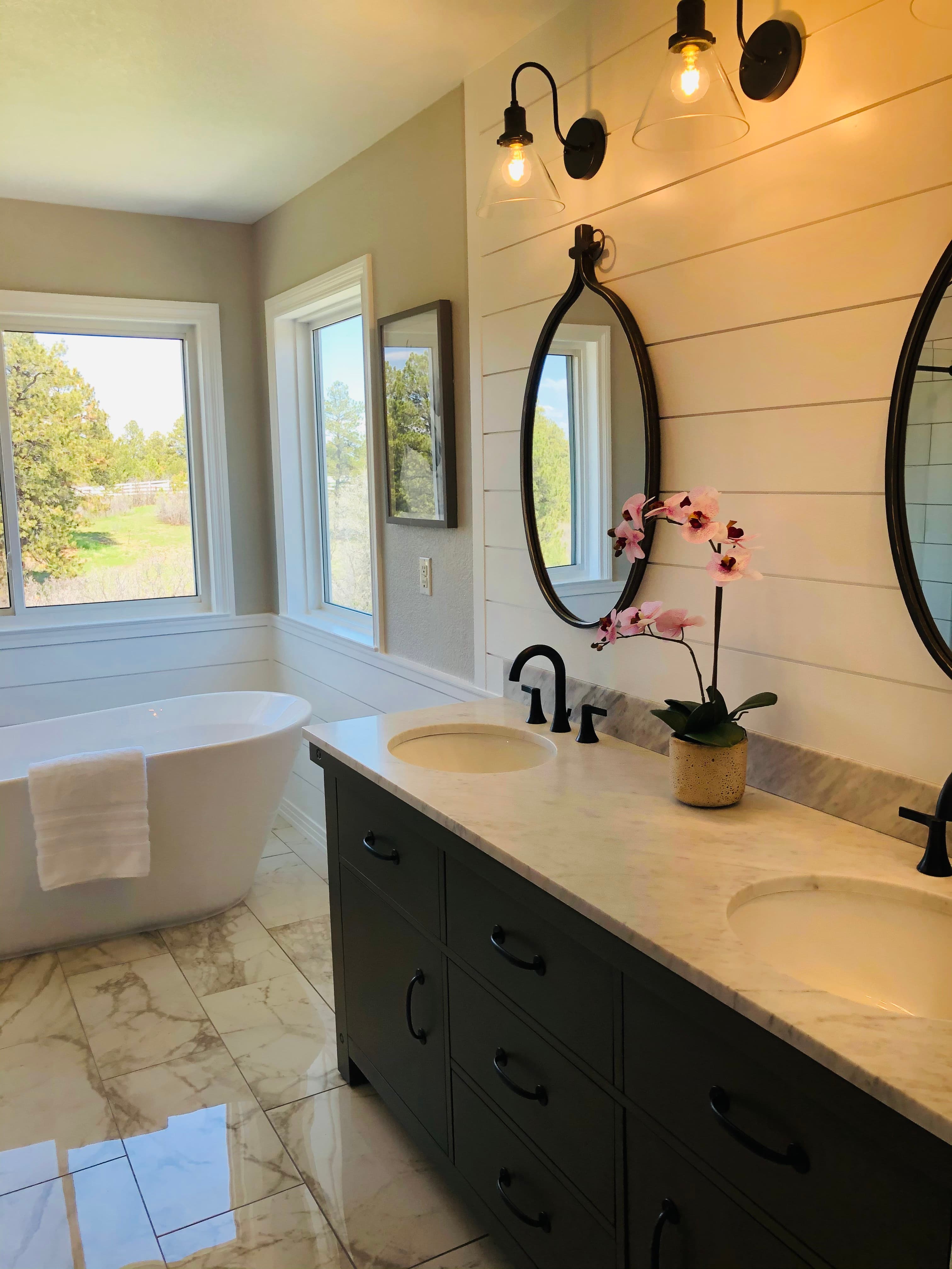 Bathroom with a freestanding white tub, a double vanity with dark cabinets and marble-look floors