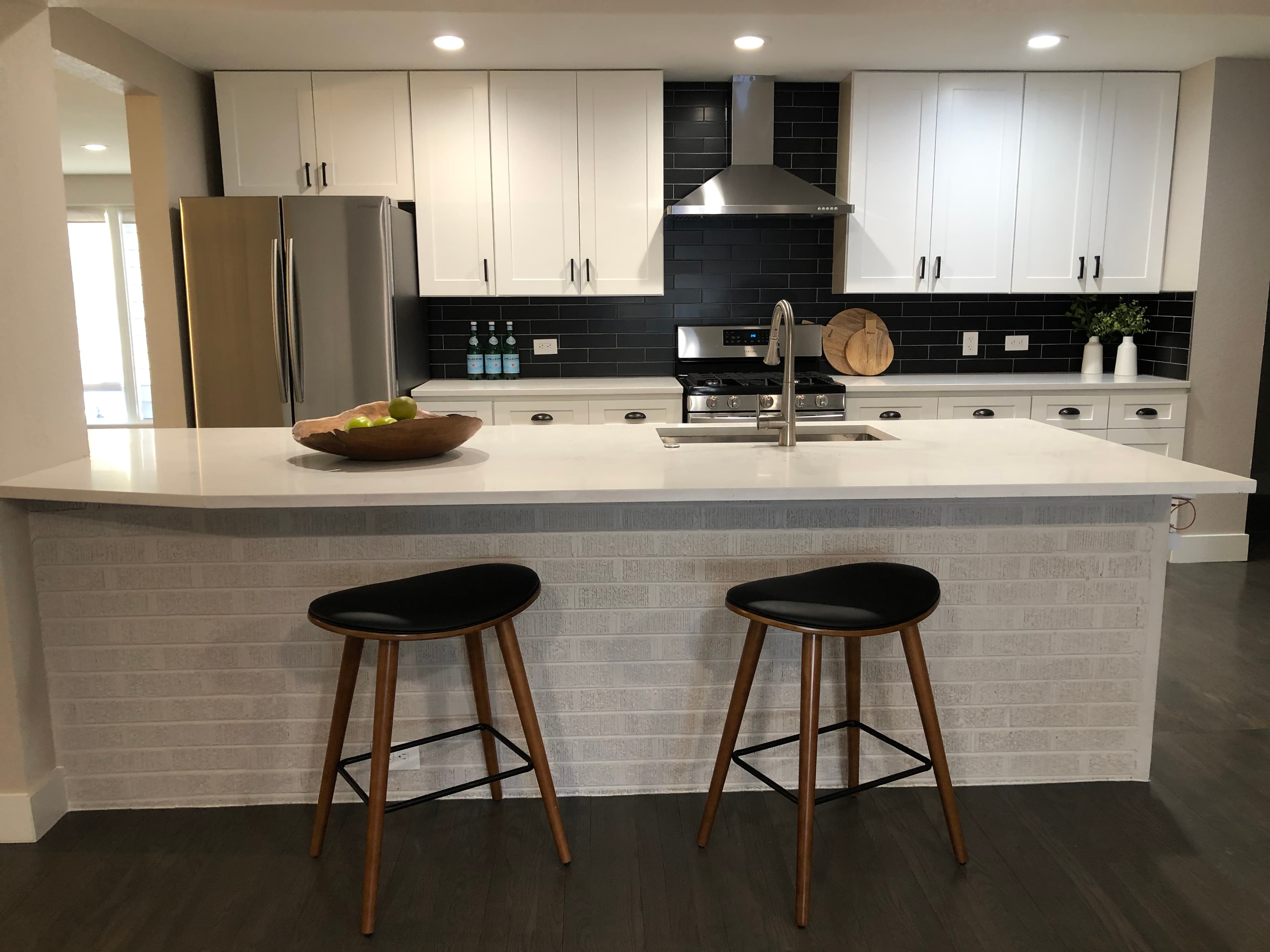 Kitchen with white shaker cabinets, a black tile backsplash and a white island with black stools